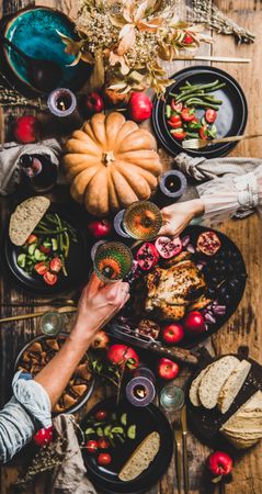 Autumnal table with squash and candles with two hands toasting with glasses of wine