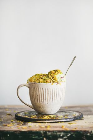 Cup of pistachio ice cream with spoon on light background