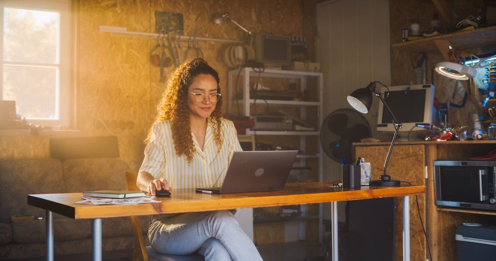 Hispanic Female Programmer Writing Code On Laptop Computer In Garage At Home.