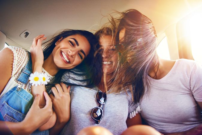 Group of female friends smiling and leaning on each other while riding in back of vehicle