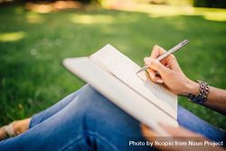 Cropped image of woman writing on a notebook sitting on green grass 5RXqDb