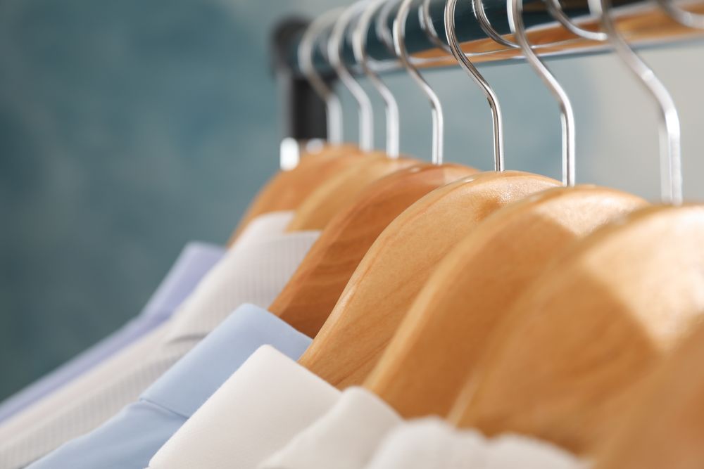 Wooden hangers with shirts against blue background, close up