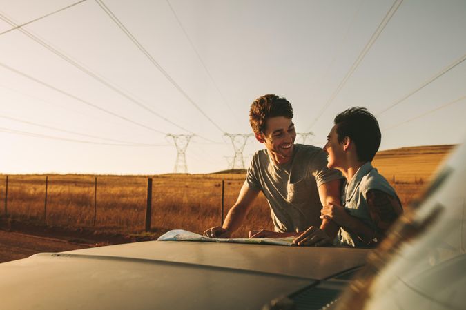 Young couple looking at each other while standing beside hood of truck on road trip
