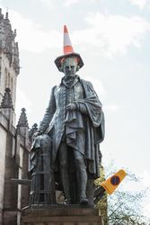 Aged monument with road cone on head