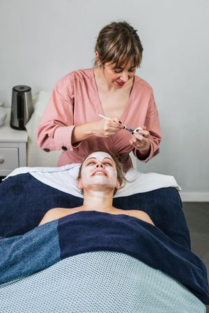 Professional beautician applying facial mask on face of client