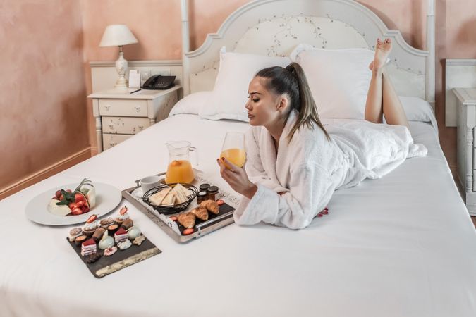 Woman in light bathrobe eating breakfast in bed in a hotel room