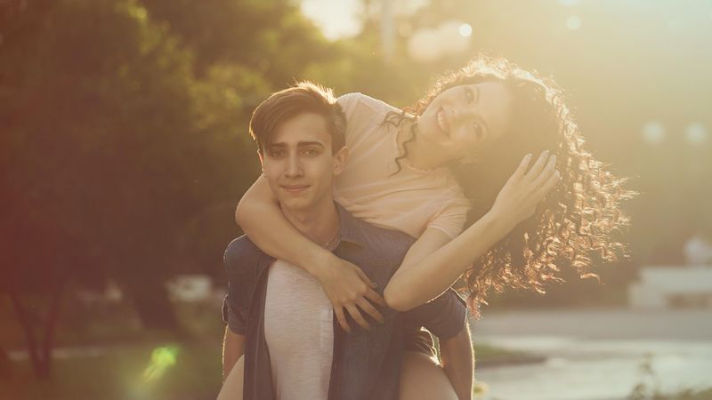 Girl with head tilted to side while piggybacking on boyfriend’s back