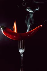 red chili pepper on fire in fork on a dark background