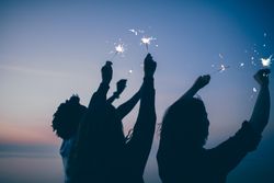 Three people hold sparklers outside at dusk