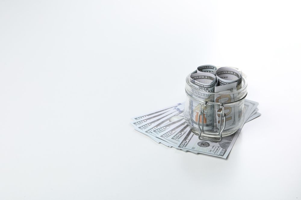 Stacks of American cash money in glass jar on light background, space for text