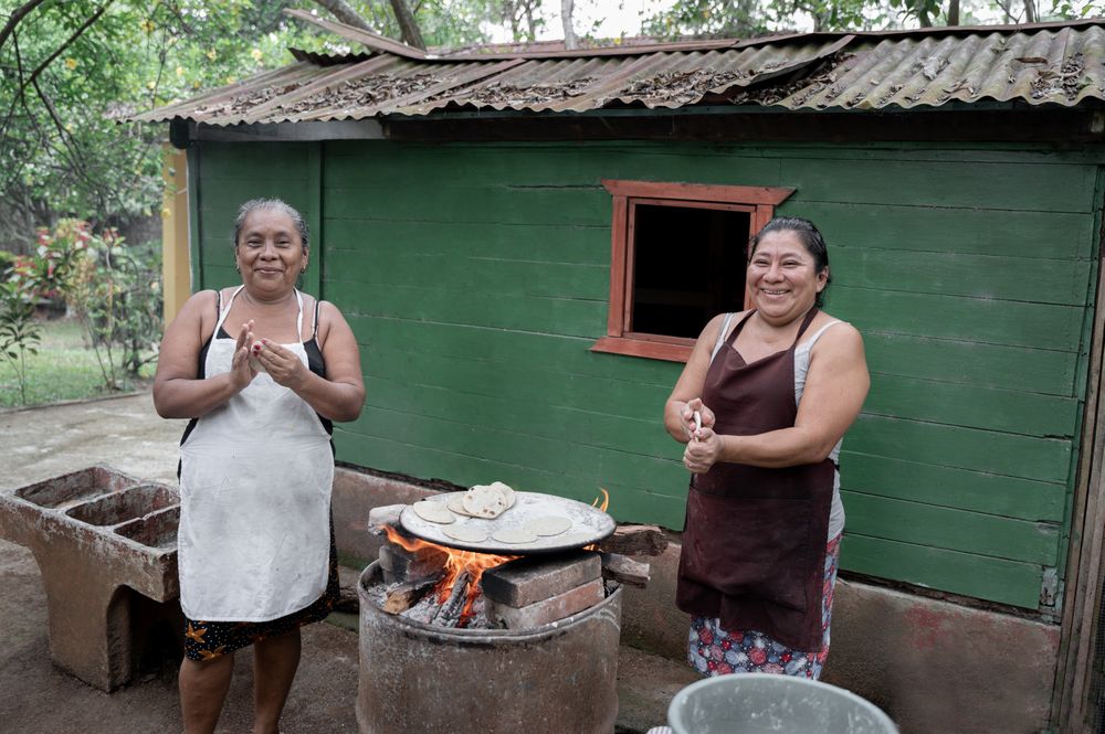 Two adult Hispanic women are smiling while shaping corn tortillas by hand