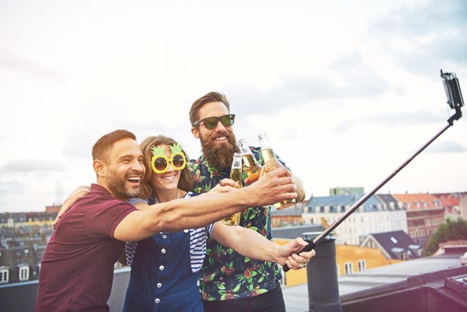 Friends having fun on a rooftop with beer and a selfie stick
