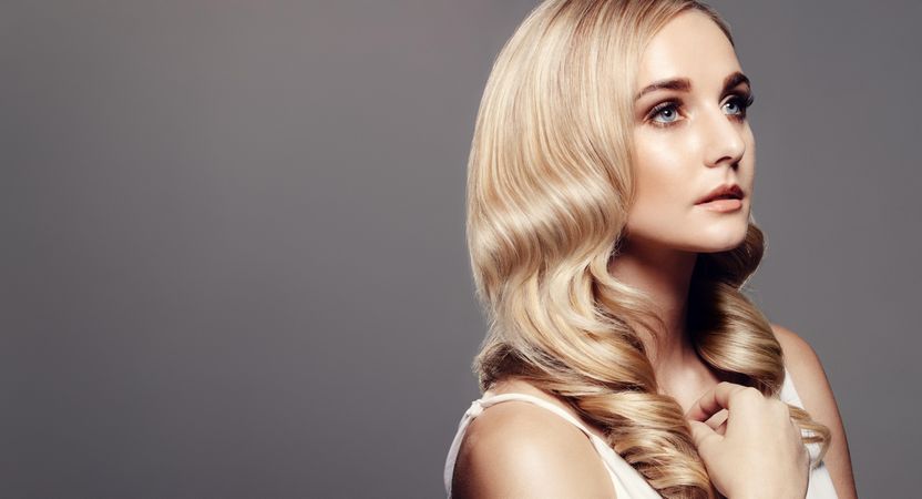 Beautiful young woman with wavy hairstyle looking away and thinking against grey background