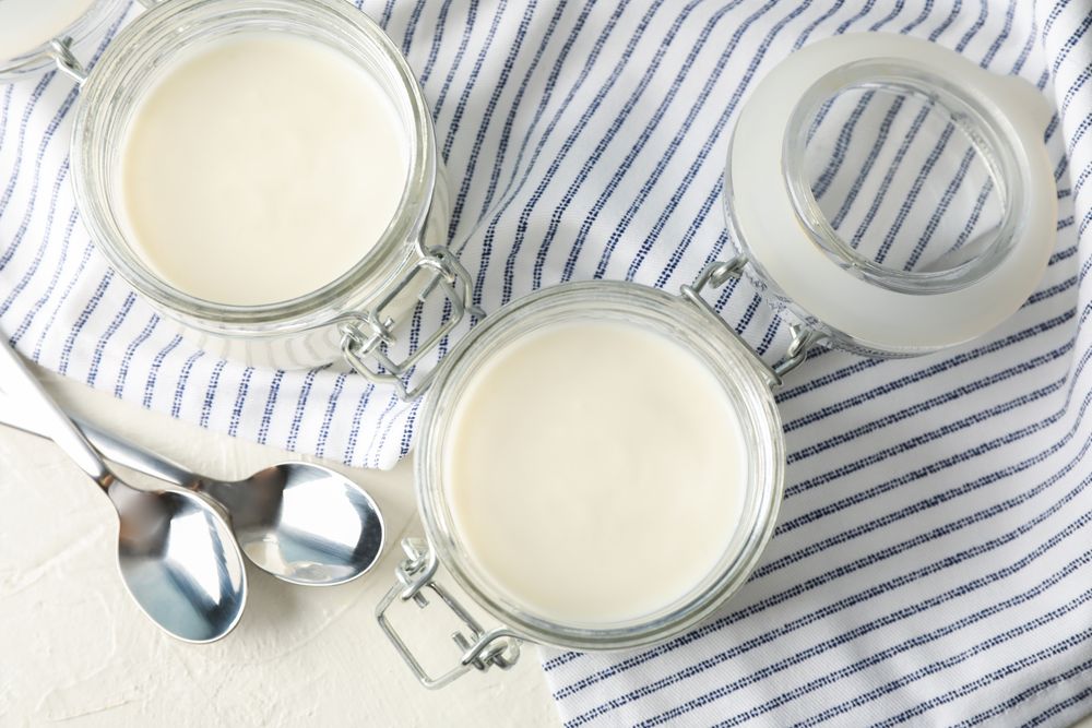 Glass jars with sour cream yogurt, spoons and towel on cement background