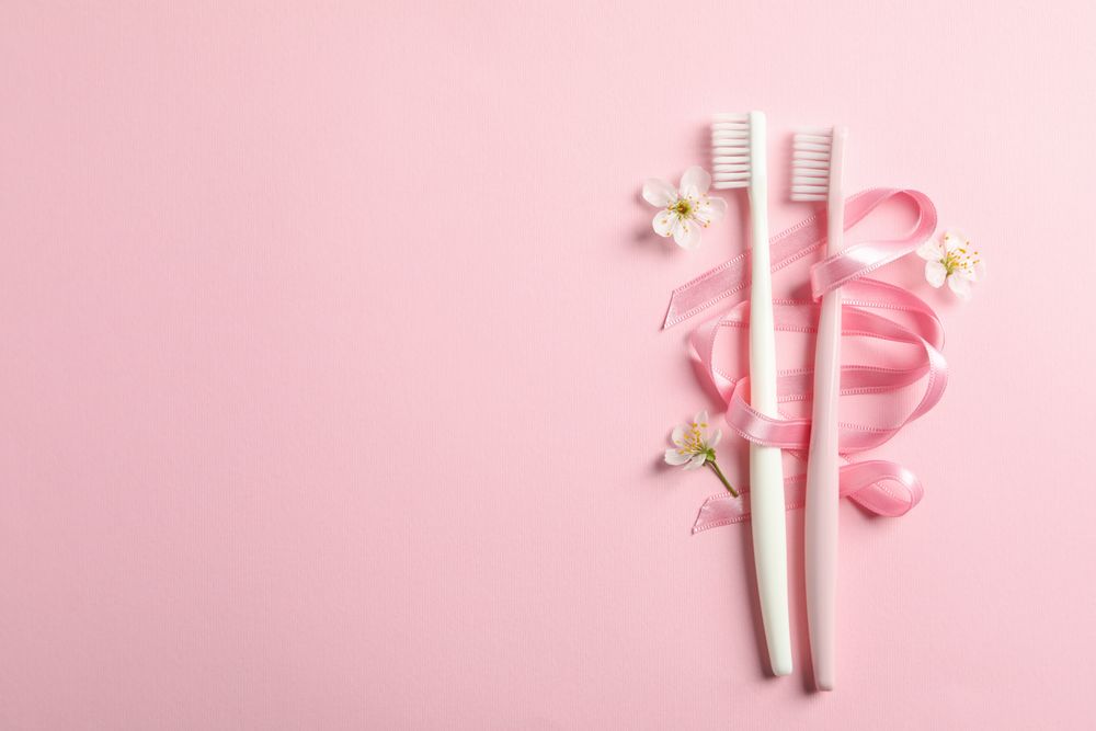 Toothbrushes, ribbon and flowers on pink background, space for text