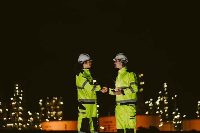 Team of two industrial workers shaking hands at night at construction site