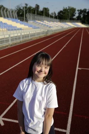 Happy child standing on running track with bleachers in the background