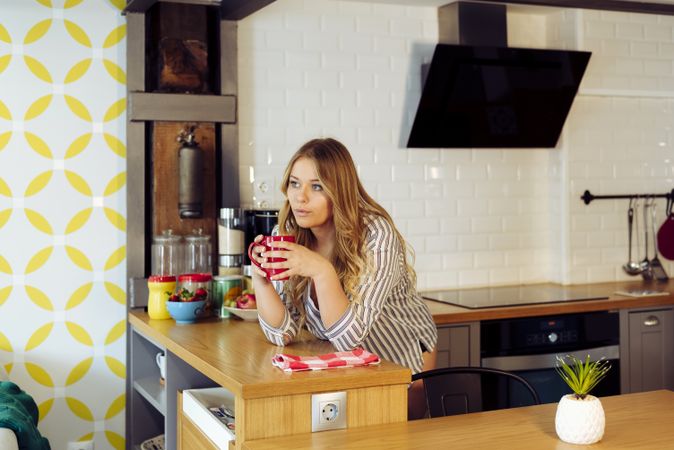 Young woman blowing on hot tea in kitchen