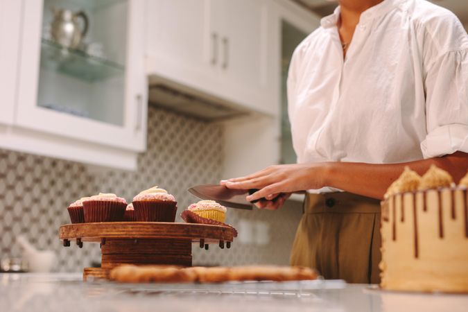 Female chef slicing cupcake on wooden board with knife in kitchen