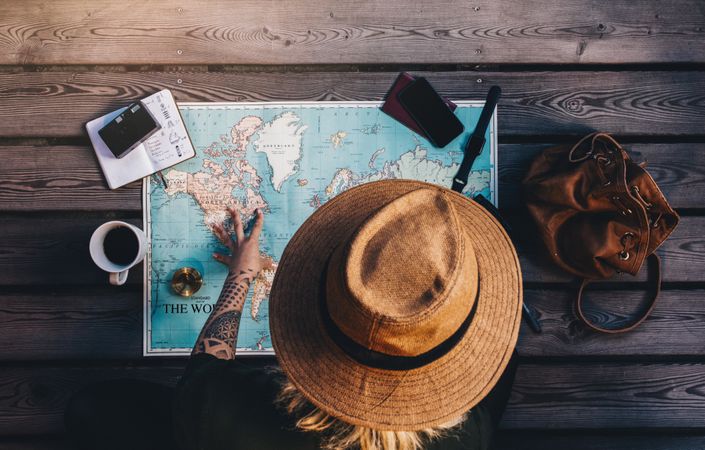Tourist exploring the world map sitting on wooden floor with compass and other travel accessories