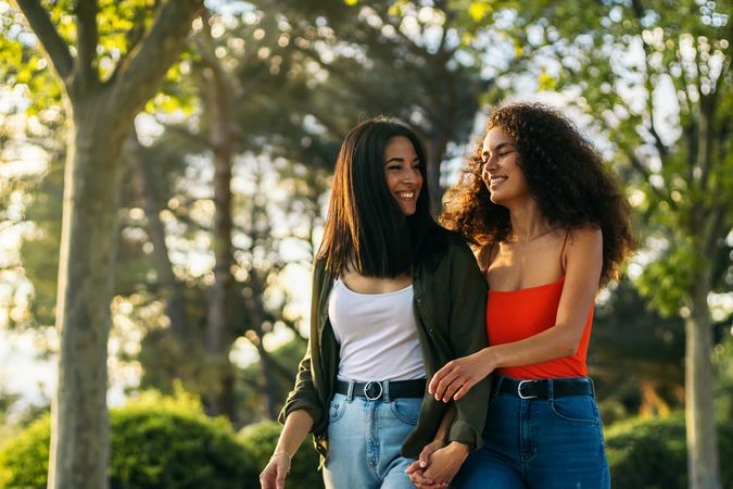 two young women, a couple, walking holding hands in a park