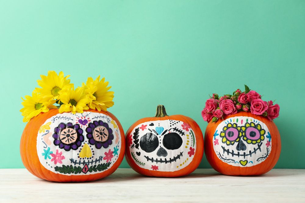 Pumpkins with catrina skull makeup and flowers on mint background