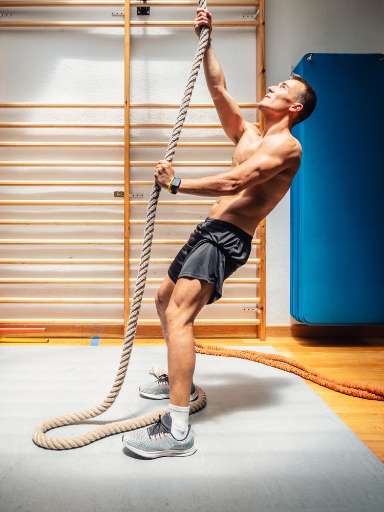 Muscular athlete climbing rope in gym