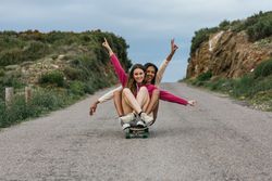 Happy diverse women riding longboard on road
