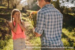 Surprised girl standing with hands on mouth looking at the flowers in the hands of her boyfriend bDWrA4