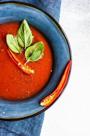 Top view of traditional Spanish soup of tomato gazpacho with basil garnish in blue bowl
