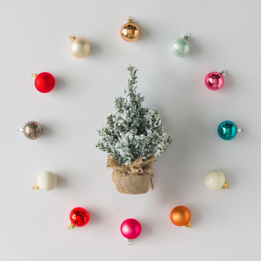 Circular border of colorful Christmas bauble decorations on light background with miniature tree