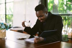 Man in blazer reading a book and drinking coffee at a coffee shop