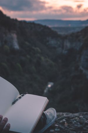 View to small river in canyon and legs of person with book sitting on the edge