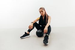 Female in athletic gear sitting on floor with ball