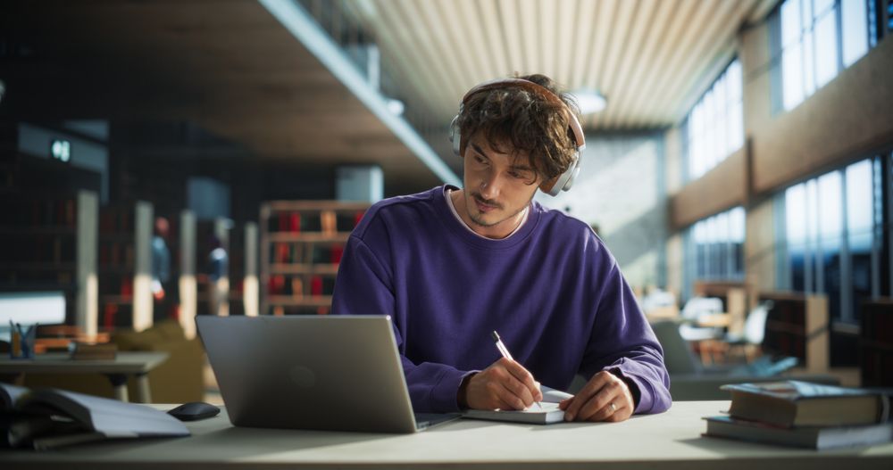 Thoughtful Young Student Preparing for Class, Doing Homework on a Laptop Computer. Freelance Journalist Working on an Article in a Public Library with Modern Simple Interior