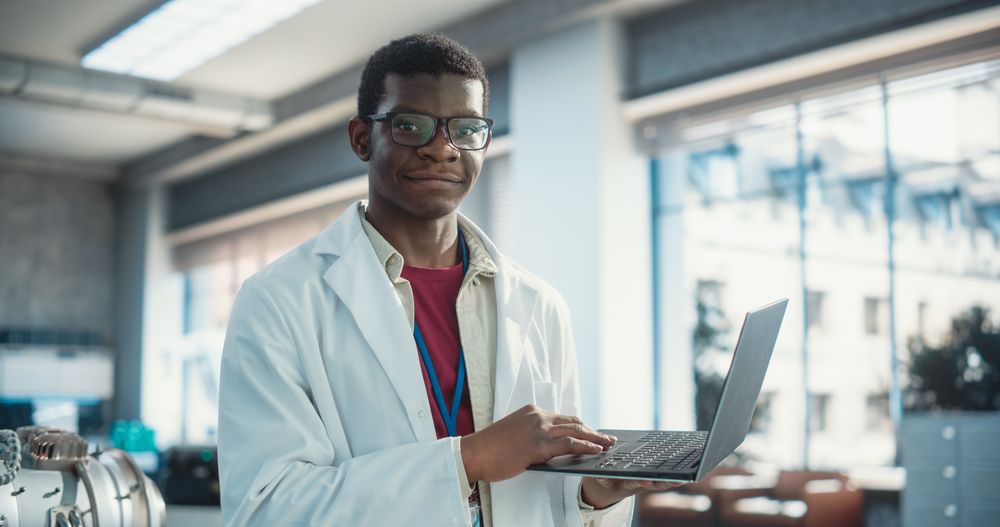 Portrait of Black Male Scientist Using Laptop Computer, Looking at Camera and Smiling in a Laboratory.