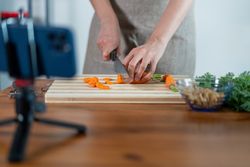 Close-up of hands slicing carrots on a kitchen countertop filming a kitchen vlog with smartphone
