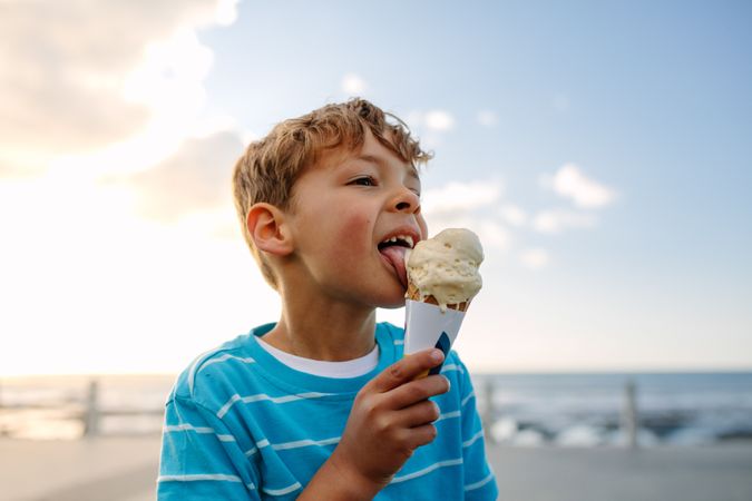 Boy licking an ice cream standing near seafront