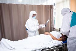 Two medical staff working with female patient in hospital bed