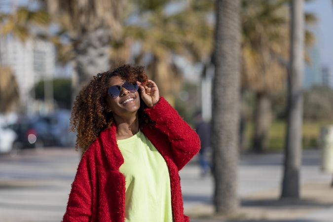 Happy female with hand to her sunglasses on street with palm trees