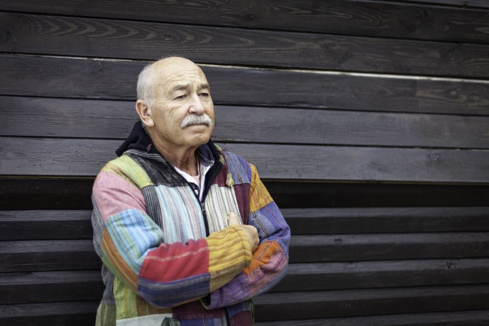 Pensive mature man with arms folded against house
