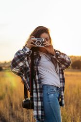 Young woman taking photos with analog camera in the field at sunset