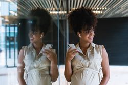 Smiling Black pregnant woman using smartphone and wireless earphones