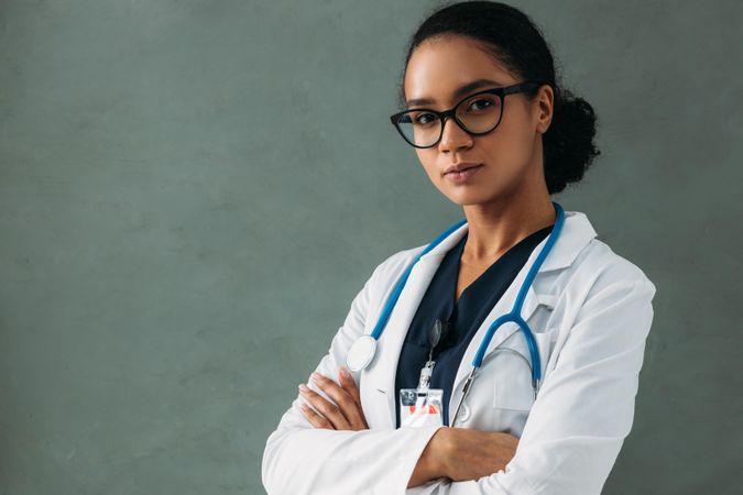 Portrait of serious female Black doctor in lab coat and stethoscope with her arms crossed