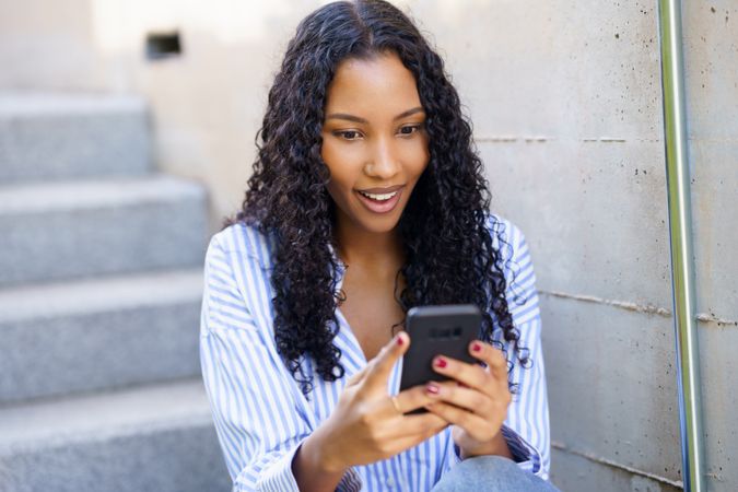 A young woman deeply engaged with her smartphone while sitting on stairs in an urban setting