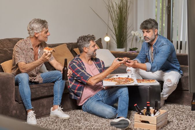 Cheerful friends eating pizza together in living room