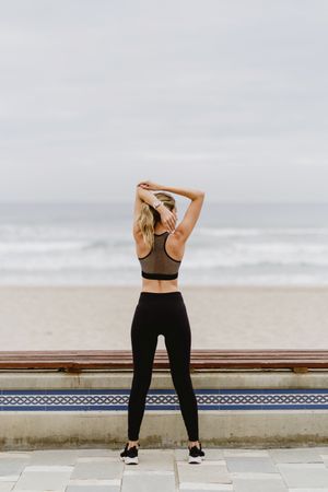 Faceless female gymnast in sports clothing stretching before exercise at seaside