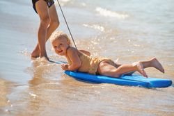 Positive toddler lying on surfboard on sandy beach