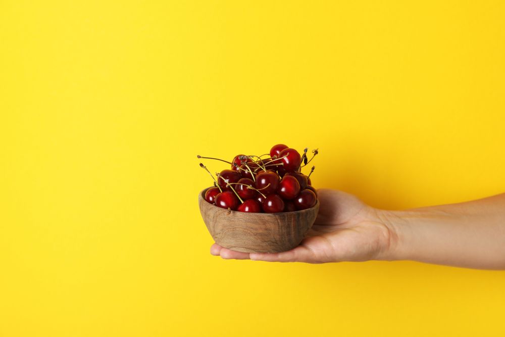 Ripe cherry fruits in a bowl on a yellow background