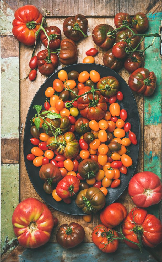 Assortment of different tomatoes in oval bowl, on wooden table, vertical composition